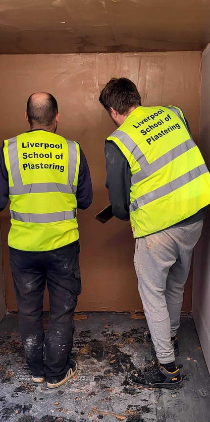 Two students in high-visibility vests practicing skimming techniques at Liverpool School of Plastering.