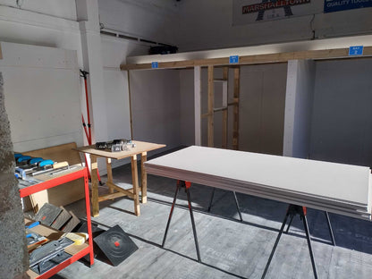 Plastering workshop showing workbench, tools, and stacked plasterboards ready for hands-on training.
