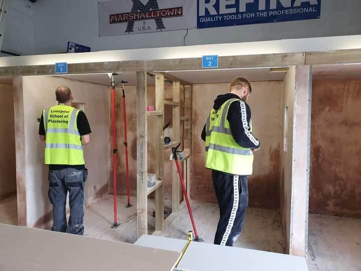 Two students practicing plaster skimming techniques in a hands-on training environment at the Liverpool School of Plastering.